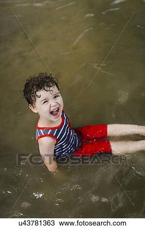 Stock Image - Smiling boy (4-5) sitting in lake. Fotosearch