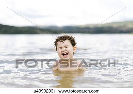 Stock Image - Smiling boy ( 4-5) swimming in lake. Fotosearch