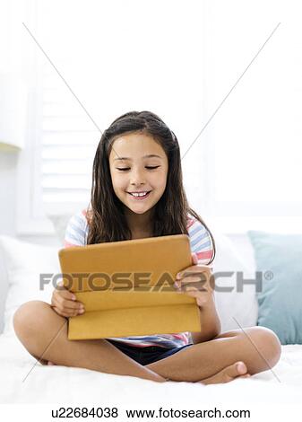 Stock Photo - Smiling girl (10-11) sitting and watching tablet. Fotosearch