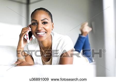 Smiling woman lying on bed and using phone View Large Photo Image Stock Photo - Smiling woman lying on bed and using phone. Fotosearch
