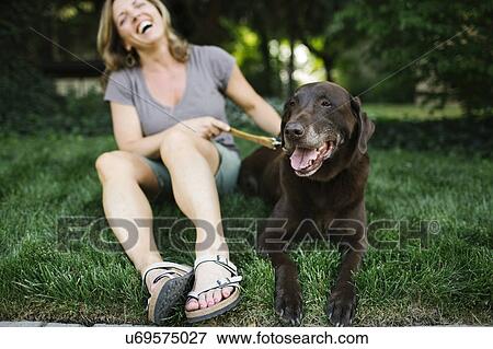 Stock Photo - Smiling woman sitting on grass with Labrador Retriever. Fotosearch