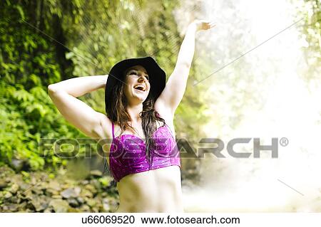 Stock Image - Smiling woman standing by waterfall. Fotosearch