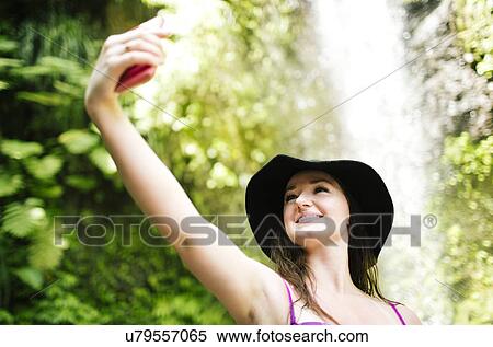 Smiling woman taking selfie with waterfall in background View Large Photo Image Stock Photography - Smiling woman taking selfie with waterfall in background. Fotosearch
