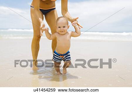 Son (12-17 months) learning to walk with mother on beach View Large Photo Image Stock Photo - Son (12-17 months) learning to walk with mother on beach. Fotosearch