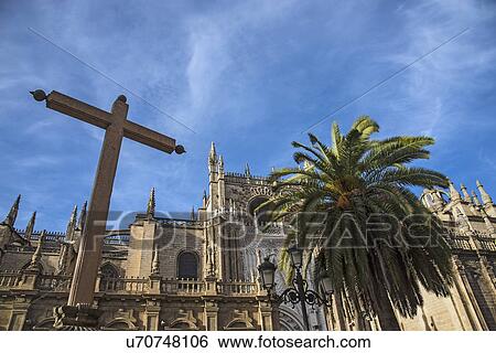 Stock Photograph - Spain, Andalusia, Seville, Cathedral of Seville with palm tree and cross in foreground. Fotosearch