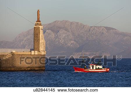 Spain, Andalusia, Tarifa, port of Tarifa, Jesus Christ statue by sea and red fishing boat View Large Photo Image Stock Photography - Spain, Andalusia, Tarifa, port of Tarifa, Jesus Christ statue by sea and red fishing boat. Fotosearch