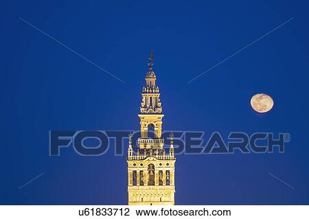 Stock Image - Spain, Seville, Giralda with full moon at dusk. Fotosearch