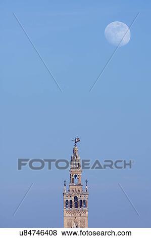 Stock Photo - Spain, Seville, Moonrise over Giralda tower at dusk. Fotosearch
