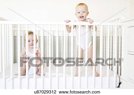 Stock Image - Twin brothers (12-17 months) playing in crib. Fotosearch