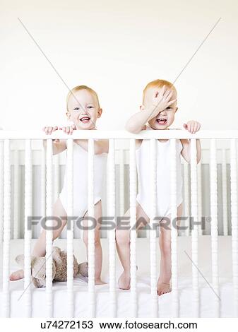 Twin brothers (12-17 months) standing in crib View Large Photo Image Stock Image - Twin brothers (12-17 months) standing in crib. Fotosearch