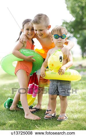 Stock Photo - Two boys (2-3, 6-7) and girl (4-5) standing with inflatable rings. Fotosearch