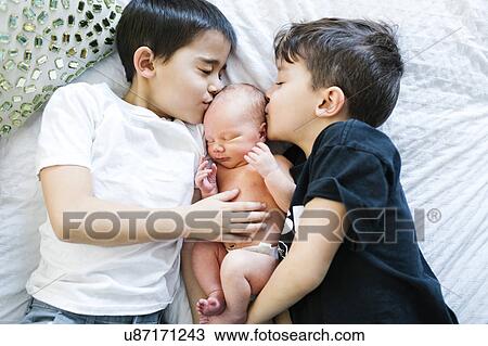 Stock Image - Two boys (6-7, 8-9) kissing baby brother (2-5 months). Fotosearch