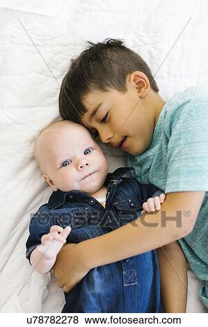 Two brothers (6-11 months) lying on bed and hugging View Large Photo Image Stock Photo - Two brothers (6-11 months) lying on bed and hugging. Fotosearch