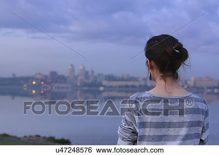 Stock Photograph - Ukraine, Dnepropetrovsk, Rear view of woman looking at city skyline at dusk. Fotosearch