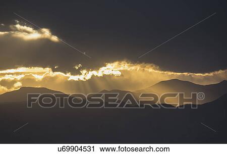 Stock Image - USA, Colorado, Denver, Dramatic sky with sunbeams over mountain range. Fotosearch