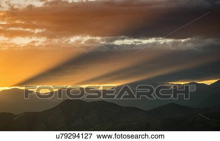 Stock Photo - USA, Colorado, Denver, Setting sun shining through clouds over Front Range. Fotosearch