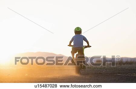 Stock Photo - USA, Colorado, Rear view of boy (8-9) cycling at sunset. Fotosearch