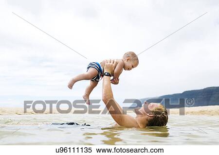 Stock Photography - USA, Hawaii, Kauai, Father with baby boy (12-17 months) playing in sea. Fotosearch