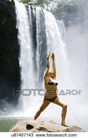 Stock Image - USA, Hawaii, Kauai, Woman practicing yoga next to waterfall. Fotosearch