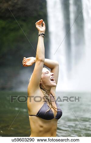 Stock Image - USA, Hawaii, Kauai, Woman wading in pond next to waterfall. Fotosearch
