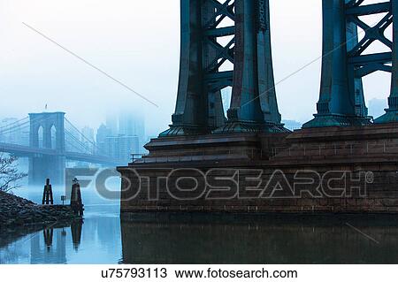 Stock Image - USA, New York, New York City, Manhattan, Brooklyn Bridge over East River in fog. Fotosearch