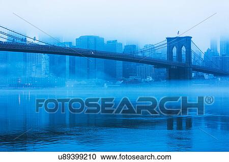 Stock Image - USA, New York, New York City, Manhattan, Brooklyn Bridge over East River in fog. Fotosearch