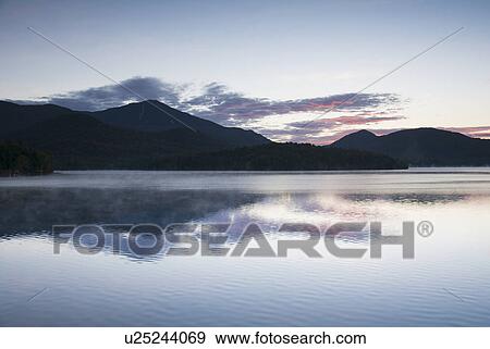 Stock Photo - USA, New York, Silhouette of mountains with Lake Placid in foreground at sunrise. Fotosearch