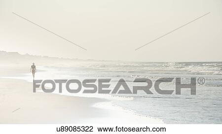 Stock Image - USA, North Carolina, Woman walking on empty beach. Fotosearch
