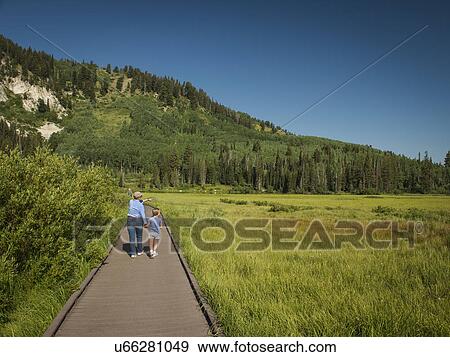 Stock Photo - USA, Utah, Lake City, Girl (4-5) with grandmother walking on boardwalk through wetland. Fotosearch