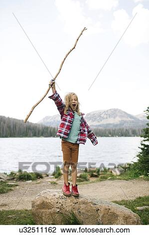 Stock Image - USA, Utah, Midway, Boy with stick (6-7) standing on rock by lake. Fotosearch