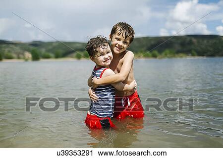 Stock Image - USA, Utah, Park City, Brothers (4-5, 6-7) embracing in lake. Fotosearch