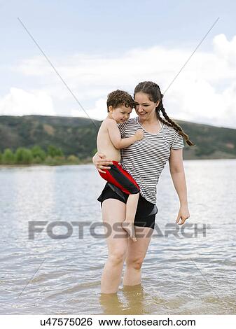 Stock Photograph - USA, Utah, Park City, Mother carrying son (4-5) while wading in lake. Fotosearch