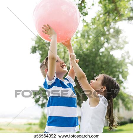 Stock Image - USA, Utah, Salt Lake City, Boy (6-7) and girl (4-5) playing with large pink ball. Fotosearch