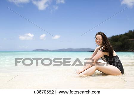 Stock Image - USA, Virgin Islands, Saint Thomas, Beautiful woman sitting on shore. Fotosearch