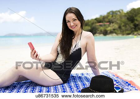 Stock Photography - USA, Virgin Islands, Saint Thomas, Woman listening to music on beach during summer vacations. Fotosearch