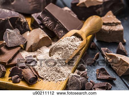 Stock Image - Various pieces of chocolate around wooden scoop with chocolate powder. Fotosearch