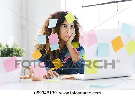 Stock Photo - Woman covered with sticky notes using laptop at table. Fotosearch