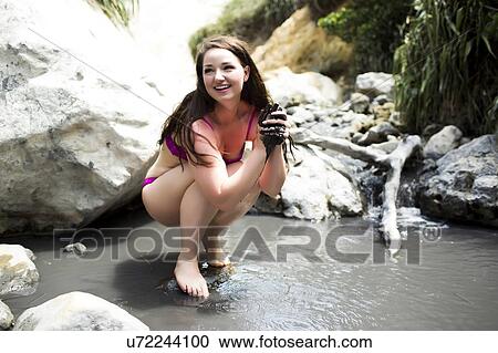 Stock Image - Woman crouching in small pond. Fotosearch