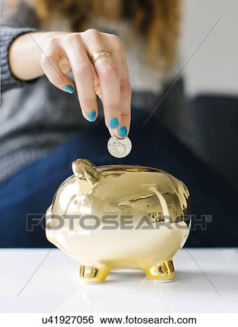 Woman dropping coin into gold piggy bank View Large Photo Image Stock Photograph - Woman dropping coin into gold piggy bank. Fotosearch