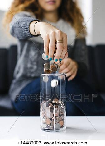 Stock Image - Woman dropping coins into glass container. Fotosearch