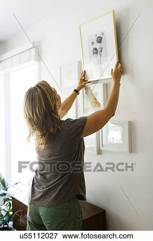 Stock Photo - Woman hanging picture frames on wall. Fotosearch