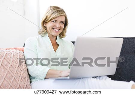 Woman holding laptop on sofa View Large Photo Image Stock Photo - Woman holding laptop on sofa. Fotosearch