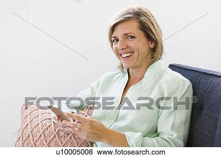 Woman holding smart phone on sofa View Large Photo Image Stock Photo - Woman holding smart phone on sofa. Fotosearch