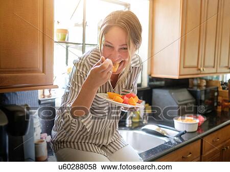 Woman in kitchen eating fruit salad View Large Photo Image Stock Photo - Woman in kitchen eating fruit salad. Fotosearch