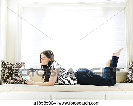 Picture - Woman lying on couch and reading book. Fotosearch