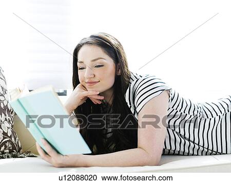 Stock Image - Woman lying on couch and reading book. Fotosearch