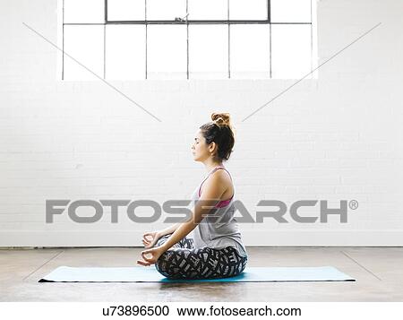 Stock Image - Woman meditating on exercise mat. Fotosearch