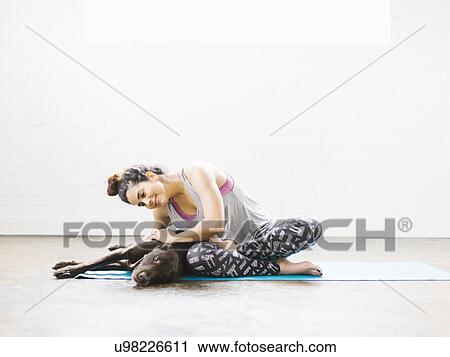 Stock Image - Woman practicing yoga with dog. Fotosearch