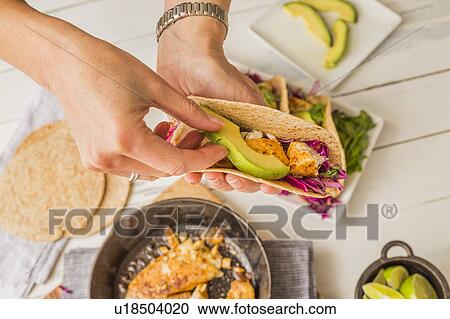 Stock Image - Woman preparing tortilla with tilapia, avocado and red cabbage. Fotosearch