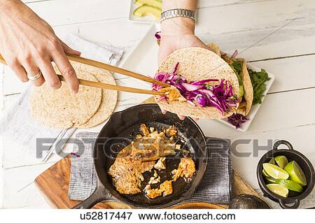 Stock Photo - Woman preparing tortilla with tilapia and red cabbage. Fotosearch